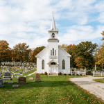White church with steeple and cemetery with tombstones surrounded by autumn trees